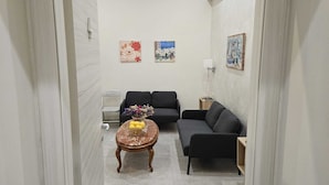 A narrow hallway leading to a living area with two sofas, a small table with flowers, and wall art. - Alloggio Turistico Port Inn (Civitavecchia)