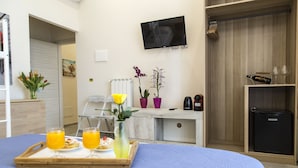 A hotel room with a bed, a tray with breakfast items, a TV, a wardrobe, and a small refrigerator. - Alloggio Turistico Port Inn (Civitavecchia)