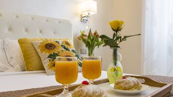 Un plateau de petit-déjeuner joliment préparé, avec des viennoiseries et du jus d’orange, posé sur un lit doté d’une tête de lit blanche et d’oreillers à motifs de tournesols.
