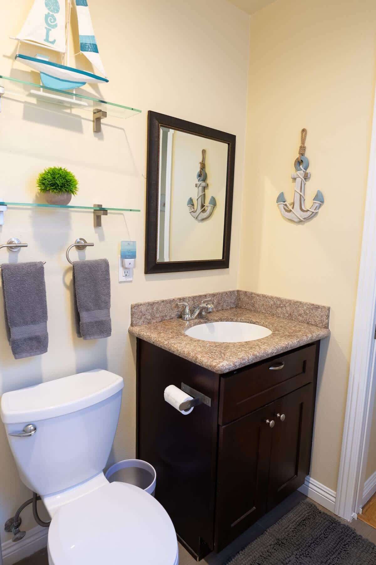 A bathroom with a white toilet, a granite sink vanity, and two towels hanging on the wall.