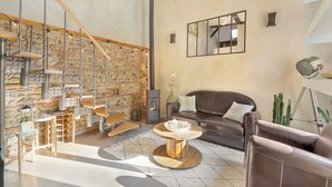 A modern living room with a stone wall, a fireplace, a brown leather sofa, and a round wooden coffee table. - LE CASTELET - Cosy duplex proche du centre-ville (Toulouse)