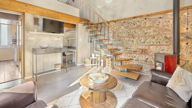 A modern living room with a stone wall, wooden staircase, and a fireplace. - LE CASTELET - Cosy duplex proche du centre-ville (Toulouse)