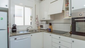 A kitchen with white cabinets, a dishwasher, a microwave, a stove, and a window with blinds.