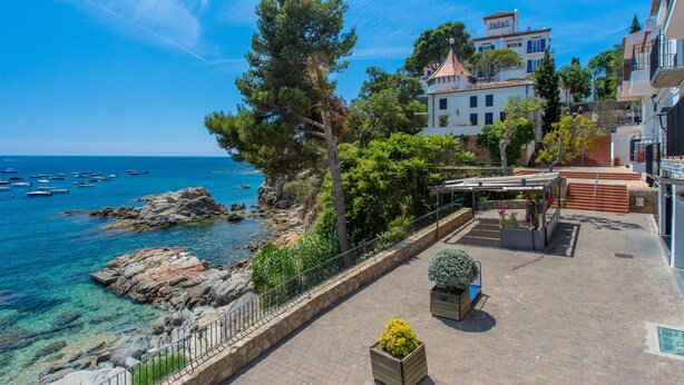 A coastal property with a patio, a view of the sea, and a building with a tiled roof.