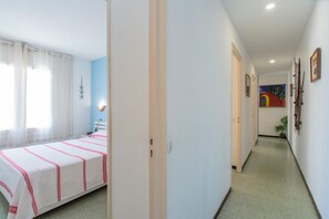 Ein Hotelzimmer mit Bett, Nachttisch und einem fenster mit Vorhängen. Ein Flur mit einer Tür, die in ein weiteres Zimmer führt.