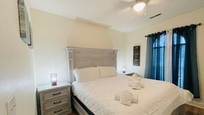 A neatly made bed with white linens and a quilted duvet, a bedside table with a lamp, and a window with curtains. - Amazing cute & cozy condo in the center of MB (Myrtle Beach)