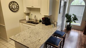 A kitchen with a granite countertop, white cabinets, a coffee station, and a potted plant. - Amazing cute & cozy condo in the center of MB (Myrtle Beach)