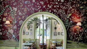 Un restaurante con un mural de aves y flores en las paredes, una mesa central grande y varias mesas con sillas.