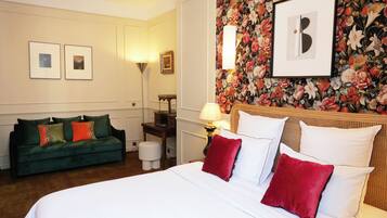 A hotel room with a bed, a green sofa, a small table, and a wall with floral wallpaper.