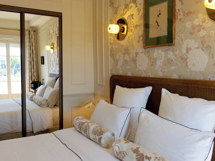 Una habitación de hotel con una cama grande, un espejo, papel tapiz floral y un cuadro en la pared.