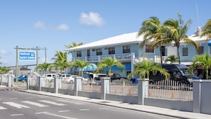 Propiedad frente al mar con un letrero que dice Nassau Yacht Haven, que presenta un edificio blanco con balcones, palmeras y coches estacionados.