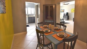 Un comedor con una mesa dispuesta para cuatro, sillas, una araña y vistas a la cocina.