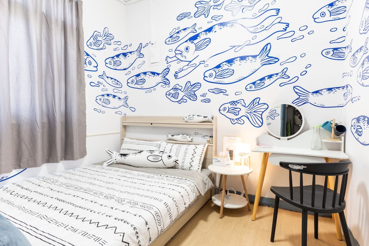 Un dormitorio con cama, escritorio y silla. La pared tiene pegatinas de peces.