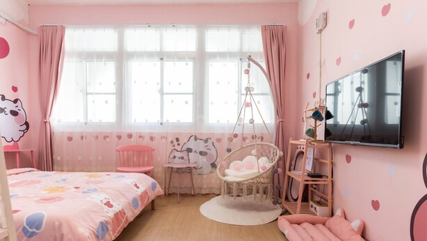 Un dormitorio con decoración rosa, una cama, una silla colgante, una mesita y un televisor.