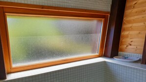 Ein Badezimmer mit satinierten Fenster, Holzbalken und einem kleinen Waschbecken mit einer Platte.