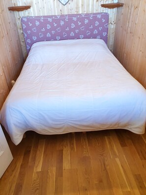 Un lit avec une tête de lit à carreaux et un matelas blanc, dans une pièce aux murs et au plancher en bois.