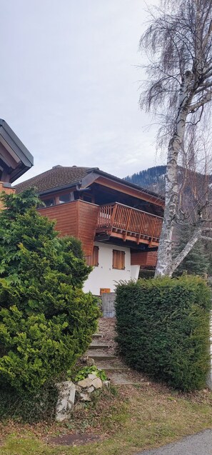 Un chalet traditionnel doté d’un toit en pente, d’un balcon en bois et d’un escalier en pierre menant à l’entrée.