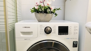 Una lavadora Samsung con tecnología digital Inverter y garantía de 10 años, ubicada en un baño con mampara de vidrio y una orquídea en maceta encima.