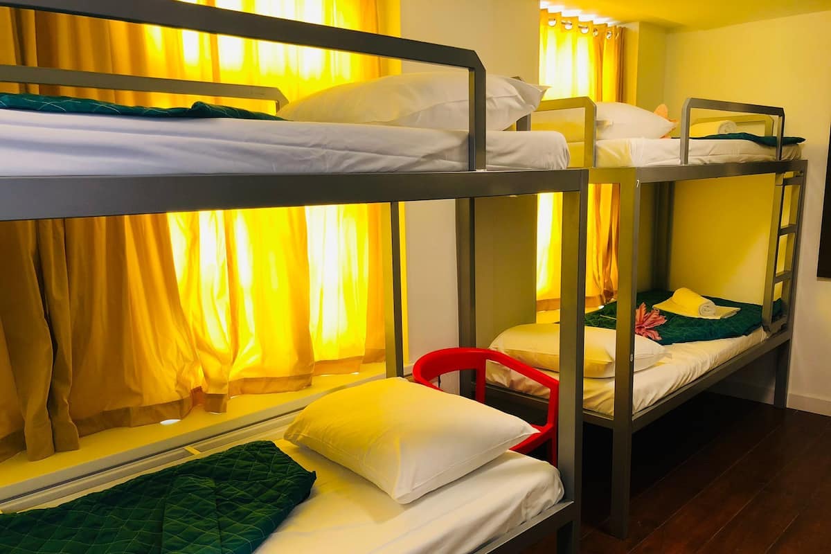 Une chambre avec un lit superposé, une chaise rouge, des rideaux jaunes et un plancher en bois.