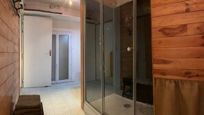 Een kamer met een houten wand, een schuifdeur naar een badkamer en een bankje in de hoek.