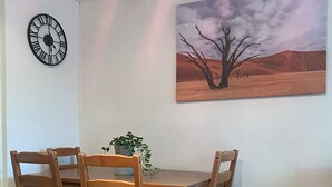 Een eetgedeelte met een houten tafel en stoelen, een klok en een landschap schilderij aan de muur.