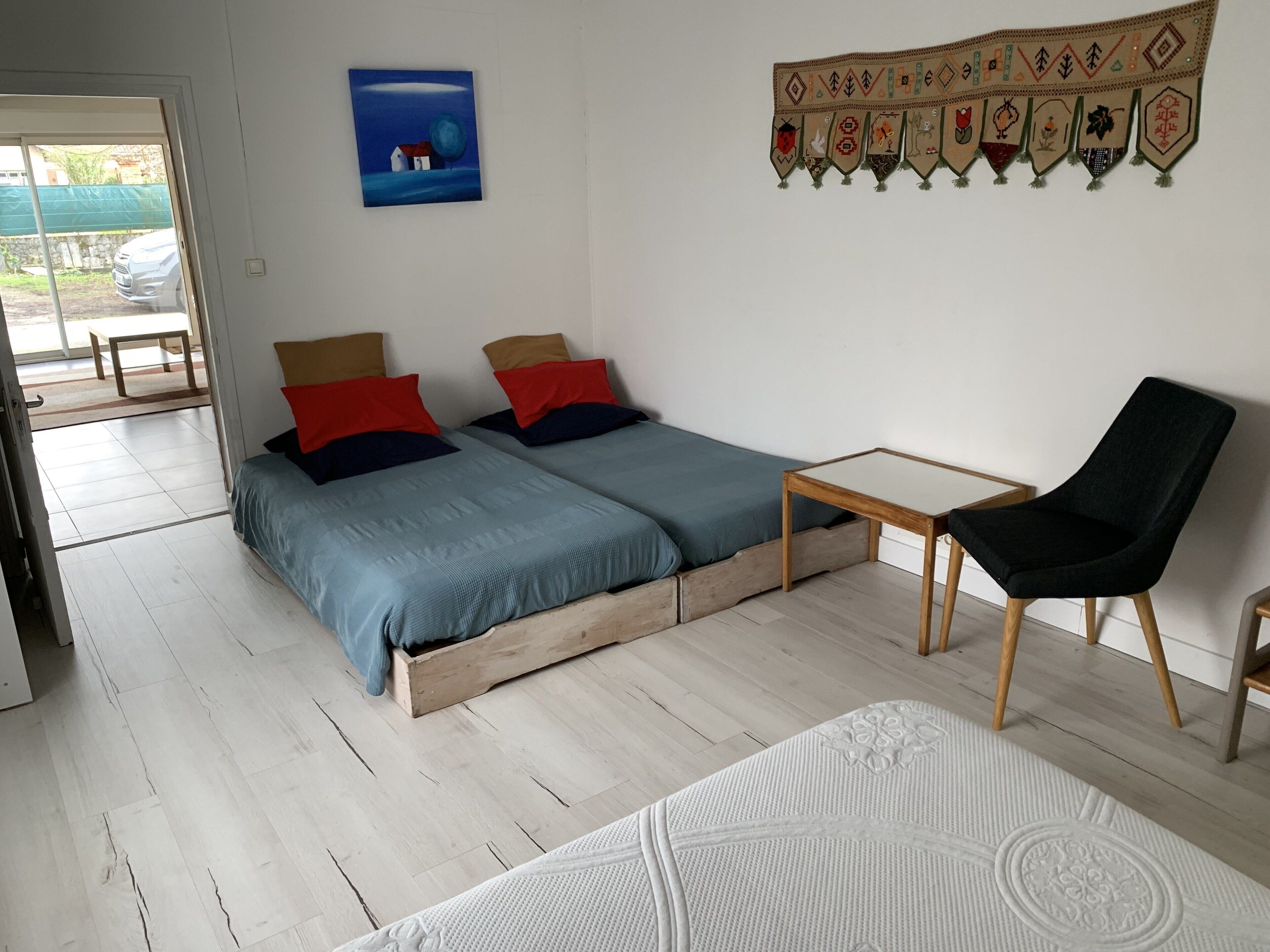 Een slaapkamer met een bed, twee kussens, een stoel, een klein tafeltje en een wanddecoratie.