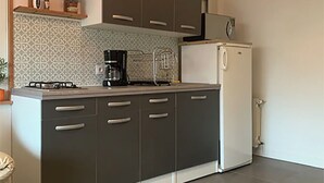 Een kleine keuken met donkere kastjes, een witte koelkast en een koffiezetapparaat.