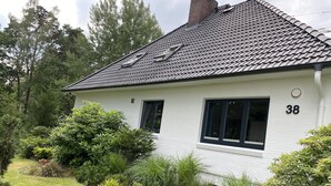 Et hvidt hus med tegltag, nummer 38, omgivet af en velholdt have med buske og græsplæne.