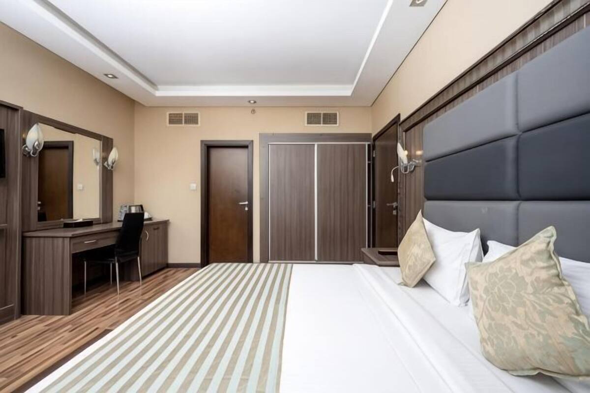 A hotel room with a bed, a desk, a chair, a wardrobe, and a mirror.