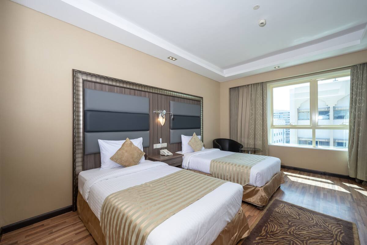 A hotel room with two beds, a large window with curtains, a desk, and a chair.