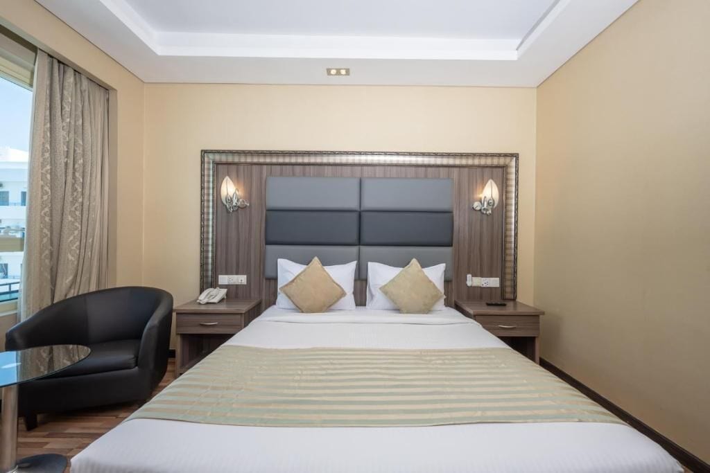A hotel room with a large bed, two bedside tables, a chair, and a view of the city.