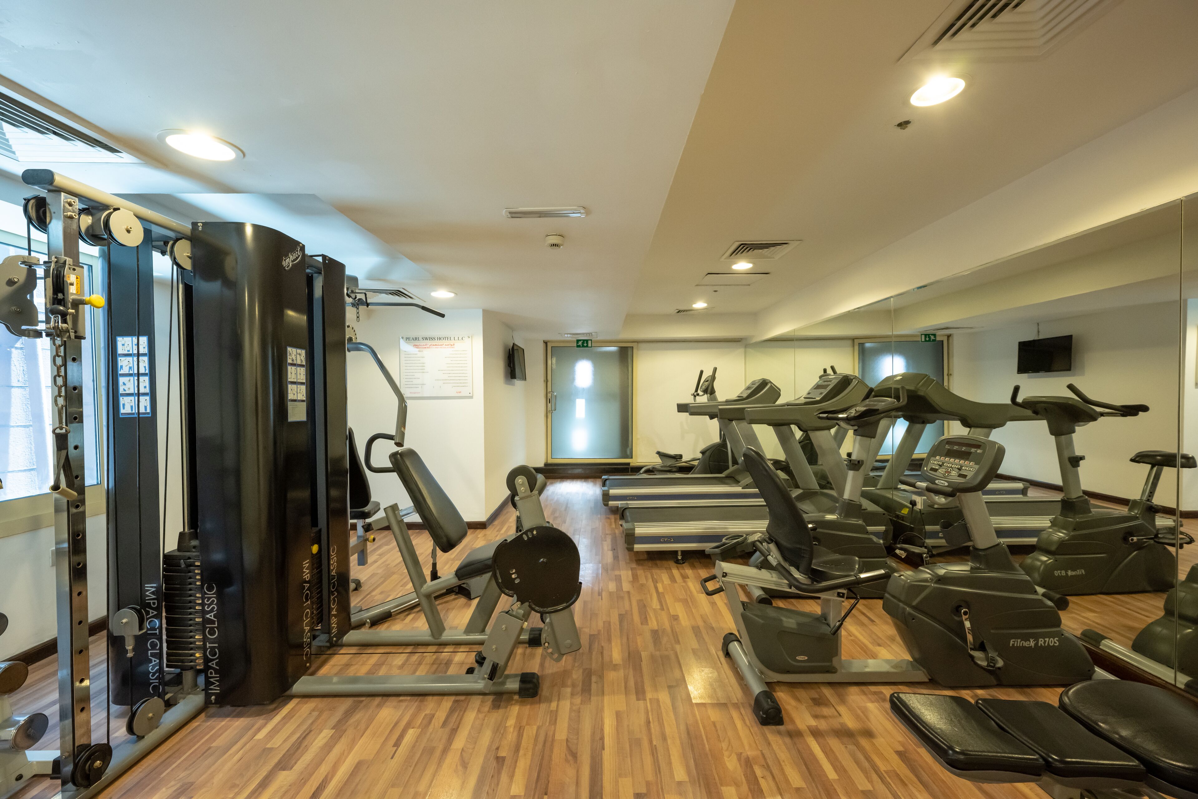 Ein Fitnessstudio mit Cardiogeräten, Krafttrainingsgeräten und Holzboden.
