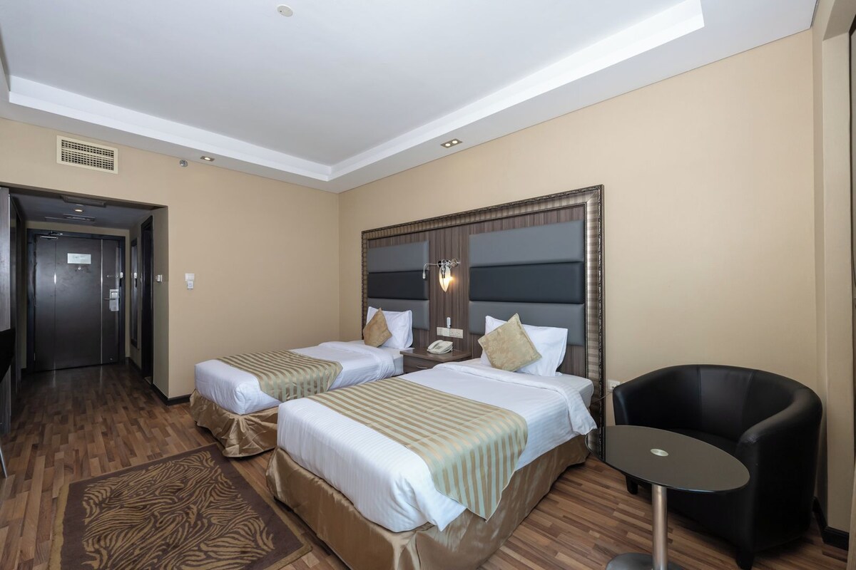 Une chambre d’hôtel avec deux lits, un coin salon et une porte donnant sur un couloir.