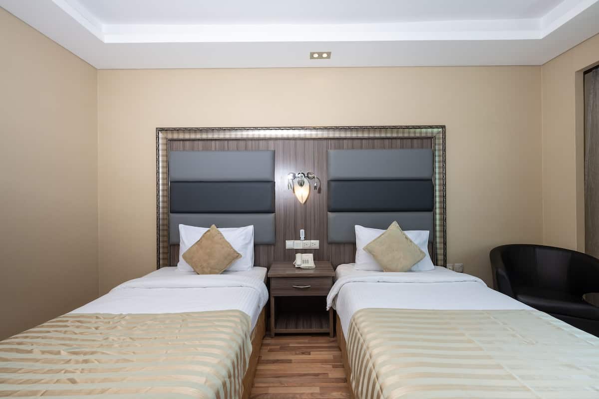 A hotel room with two beds, a nightstand with a telephone, and a chair.