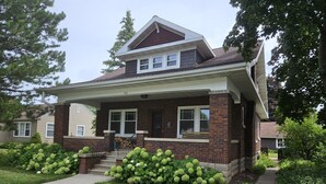 Une maison à deux étages avec une façade en briques, un porche à l’avant et une pelouse bien entretenue.