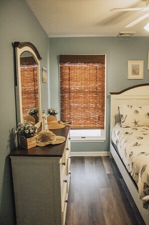 Une chambre à coucher comprenant un lit, une commode, une fenêtre avec des stores et un miroir.