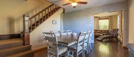 A dining area with a wooden table and chairs, a staircase, and a ceiling fan.