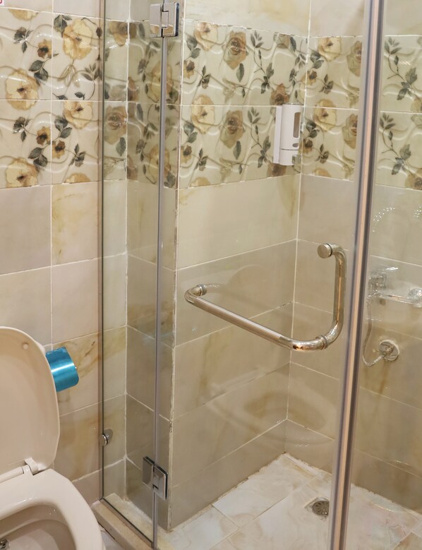 A bathroom with a glass shower enclosure, a toilet, and a handrail.