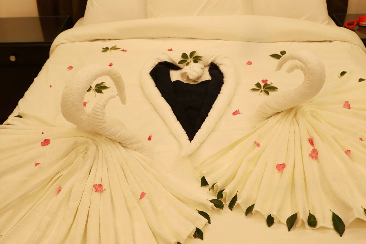 A bed with a white bedspread featuring swan and heart designs, a black pillow, and a brown curtain in the background.