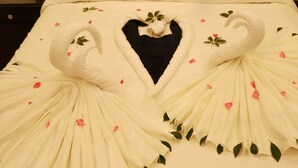 A bed with a white bedspread featuring swan and heart designs, a black pillow, and a brown curtain in the background.