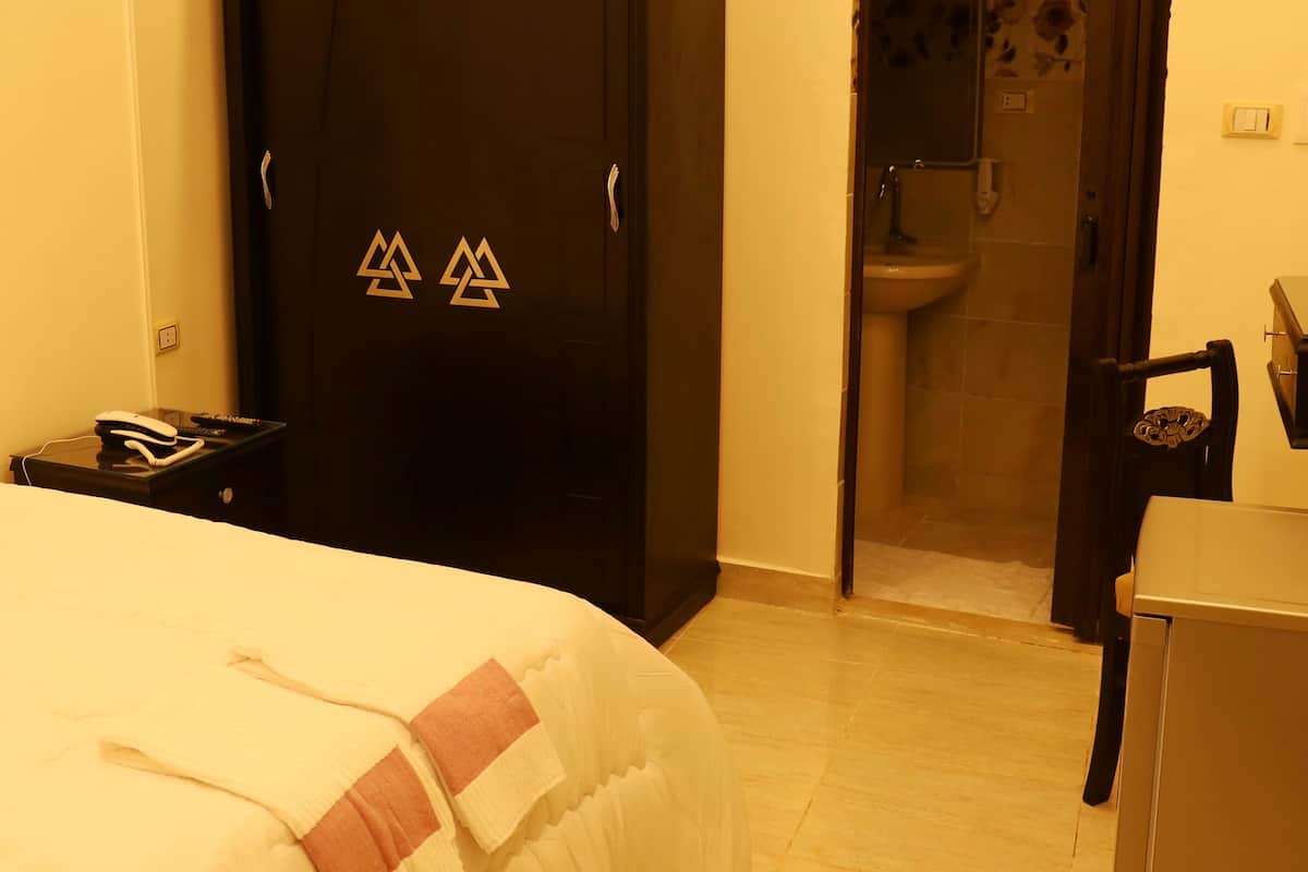 A hotel room with a bed, a desk, a chair, a wardrobe, and a bathroom visible through an open door.