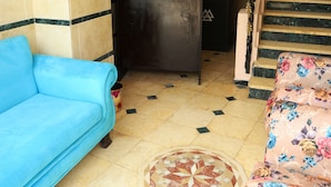 A blue sofa and a floral armchair in a room with tiled flooring and a patterned rug.