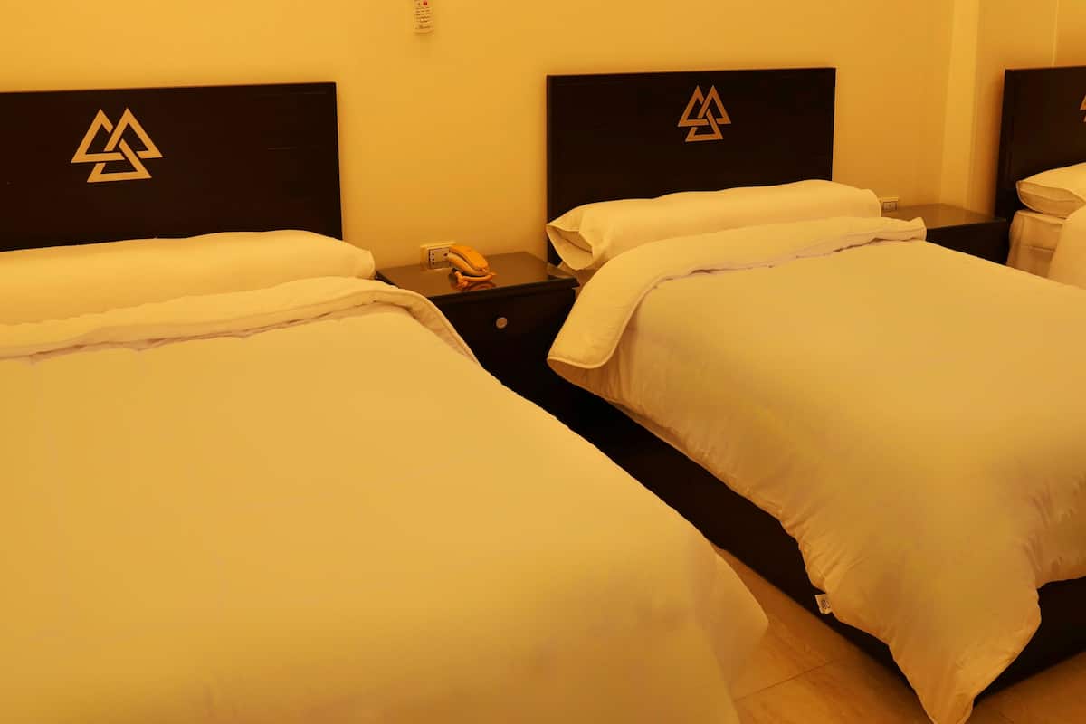 A hotel room with three beds, each with a black headboard featuring a geometric logo.