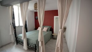 A bedroom with a bed, curtains, a red wall, and a small round table. - Large studio near the ancient theater in Orange (Orange)