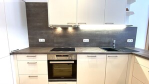 Moderni keittiö, jossa on valkoiset kaapit, musta uuni, sisäänrakennettu astianpesukone ja ruostumattomasta teräksestä valmistettu työtaso.