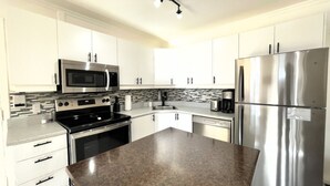 A modern kitchen with stainless steel appliances, white cabinetry, and a granite countertop.