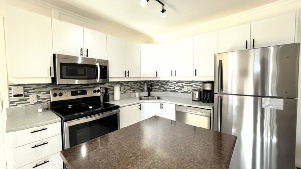 A modern kitchen with stainless steel appliances, white cabinetry, and a granite countertop. - Amazing Loft in Saint-Roch (Québec)