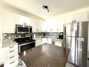 A modern kitchen with stainless steel appliances, white cabinetry, and a granite countertop.