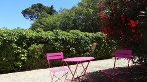 A garden with a gravel path, two pink folding chairs, and a small round table.