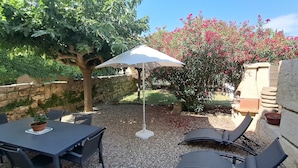 Une terrasse extérieure avec une table et des chaises, un grand parasol et un arbre aux fleurs roses.